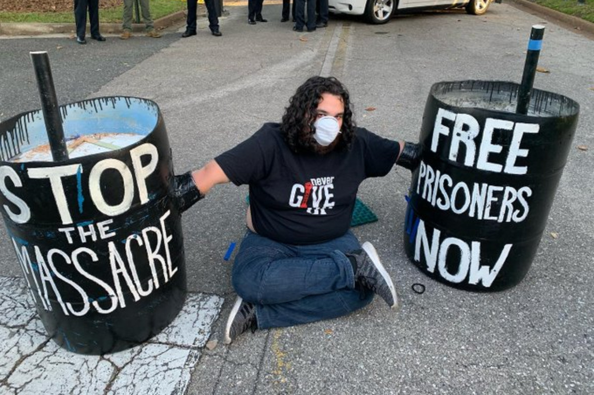 Activist Chains Self to Barrels in Front of Governor’s Mansion to Demand Release of Prisoners At Risk of COVID-19